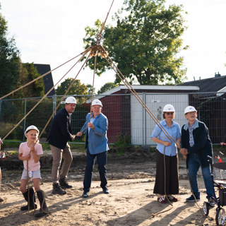 Bewoners en bestuurders slaan samen symbolisch de eerste paal om de bouwstart officieel in te luiden. 